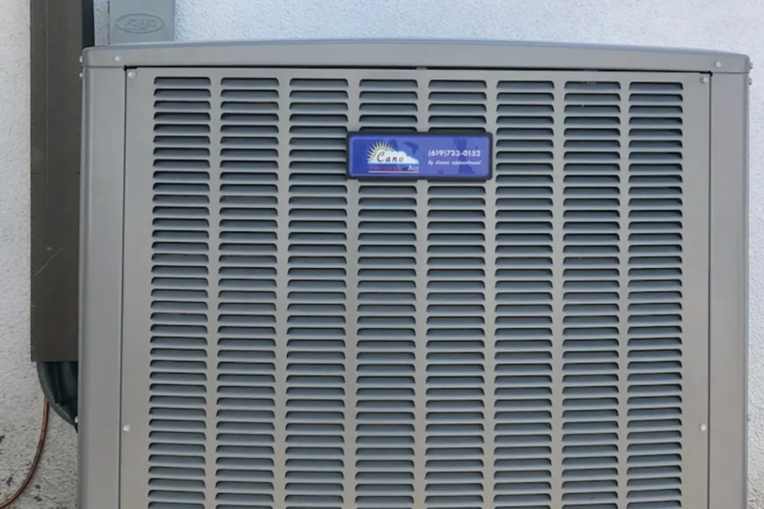 An outdoor air conditioning unit with a blue and white label that says "Cano Air (619) 733-0152 by online appointment"